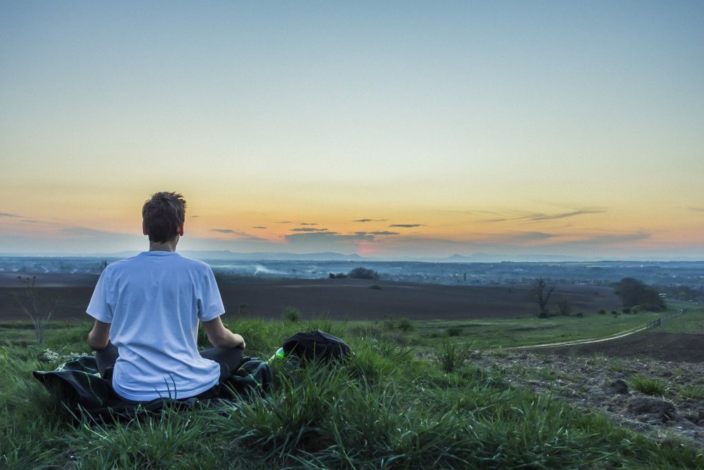 A man sits in a field and meditates at sunset.